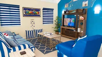 Uma sala de estar com sofá, mesa de centro, televisão e estante de livros.