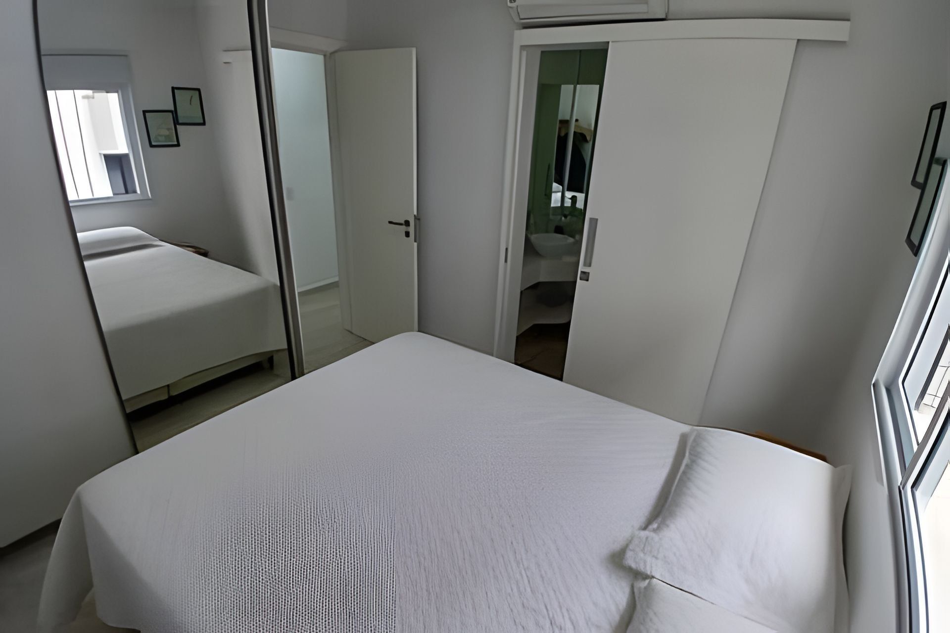 Un dormitorio con cama, armario y baño visible a través de una puerta abierta.