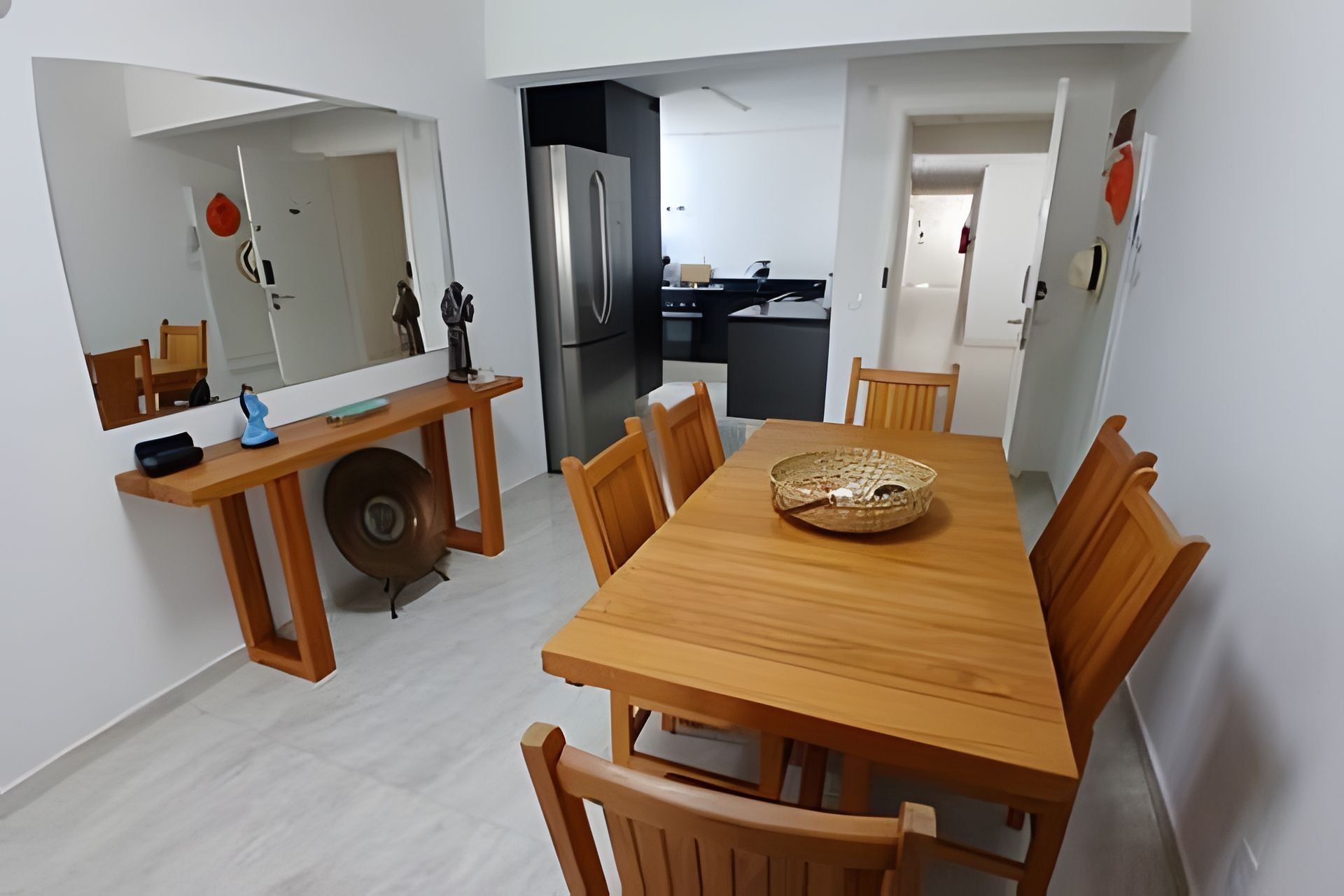 Un comedor con mesa y sillas de madera, una cocina al fondo y un espejo en la pared.