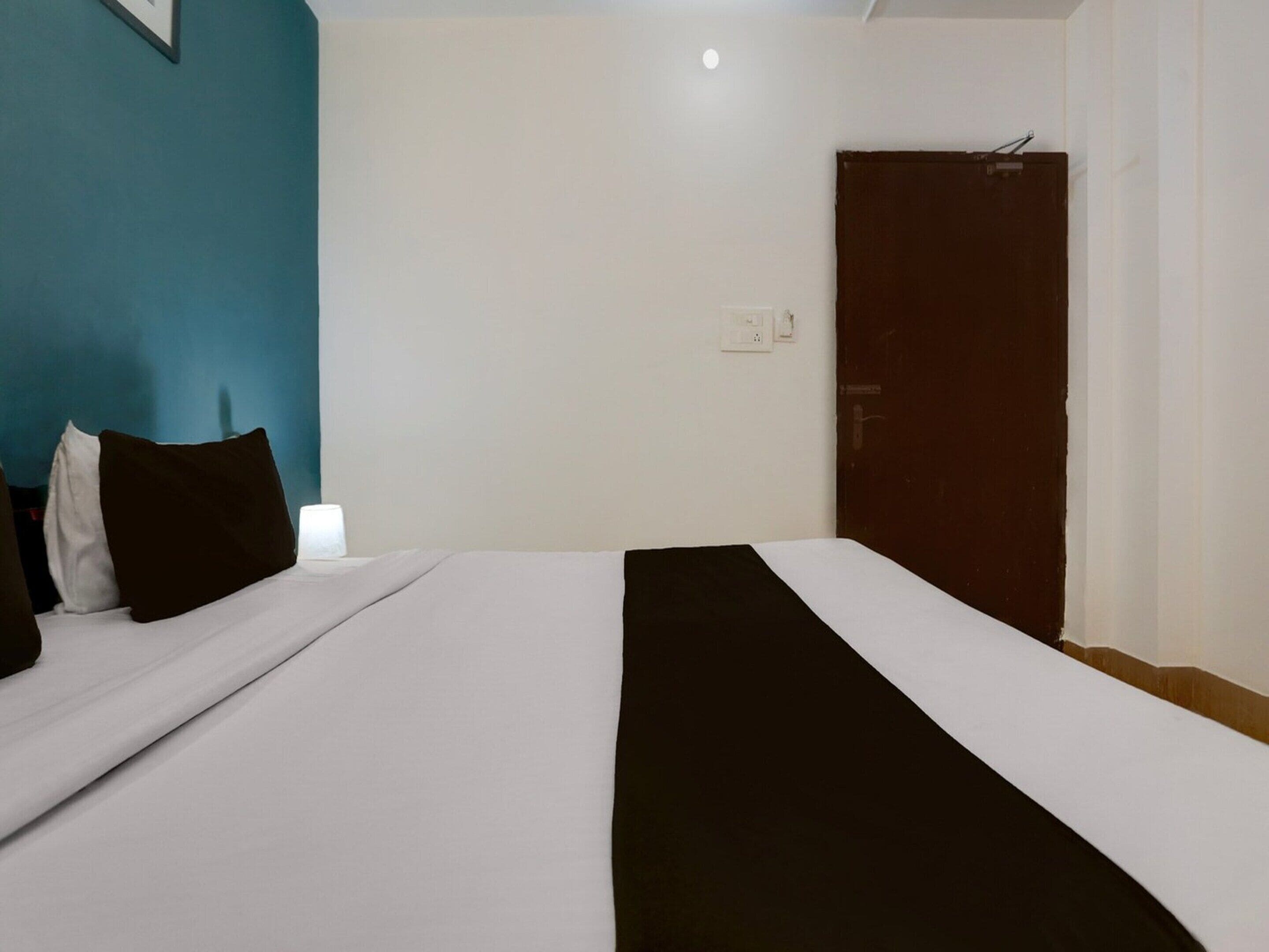 A hotel room with a bed, a nightstand, a wall socket, and a door.