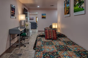 A hotel room with a bed, a desk, and a chair. There are posters on the walls.