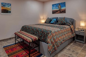 Un dormitorio con cama, banca, mesitas de noche y un cartel en la pared.