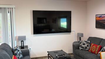 A modern living room with a flat-screen TV, two grey sofas, a coffee table, and a patterned rug.