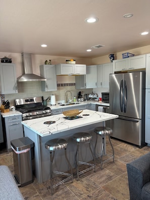 A modern kitchen with a central island, stainless steel appliances, and bar stools.
