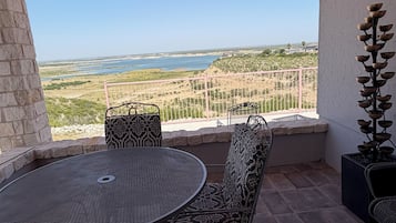A patio with a round table and chairs, a decorative plant, and a view of a coastal landscape.