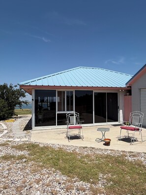 A covered patio with two white metal chairs and a small table, overlooking a body of water.