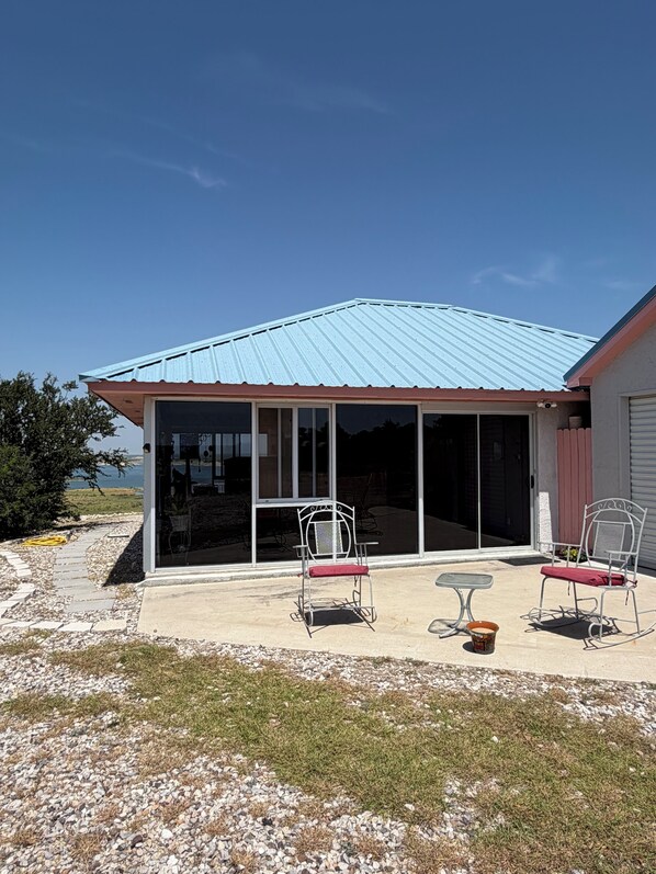 Un patio cubierto con dos sillas de metal blanco y una pequeña mesa, con vistas a una masa de agua.