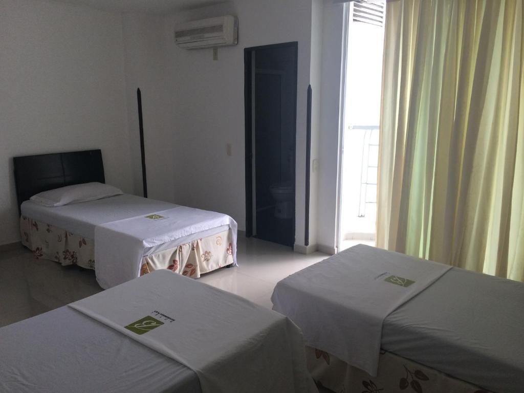 Ein Hotelzimmer mit zwei Einzelbetten, einem dunkel gefärbten Kopfteil, einem Fenster mit Vorhängen und einer Klimaanlage an der Wand.