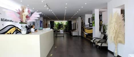 A modern hotel lobby with a reception desk, seating area, and decorative plants.