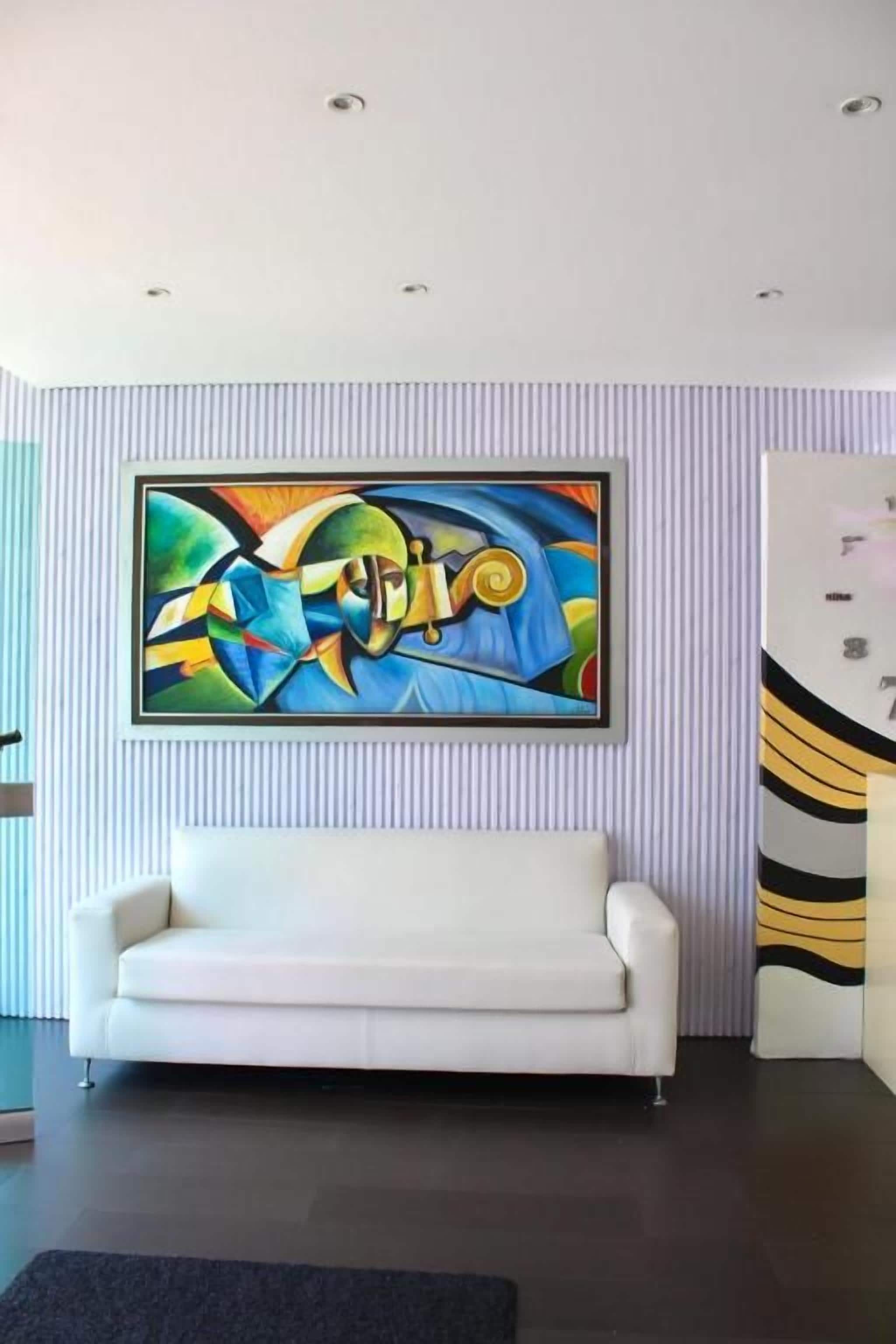 A modern interior with a white sofa, a colorful abstract painting, and a striped wall.