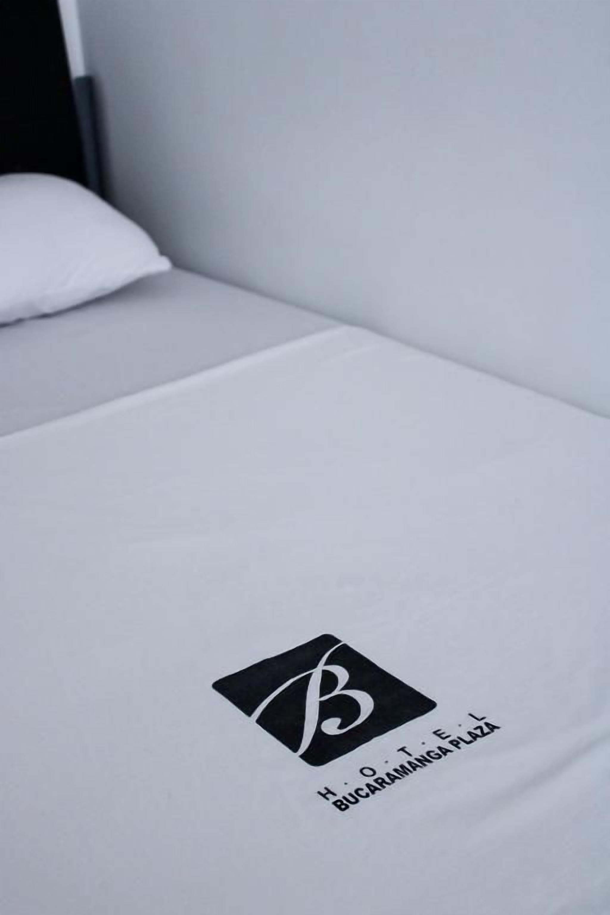 A neatly made bed with a logo and text indicating a hotel name.