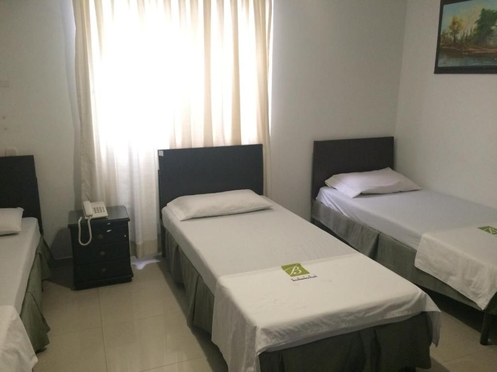 A hotel room with two single beds, a bedside table with a phone, and a window with curtains.