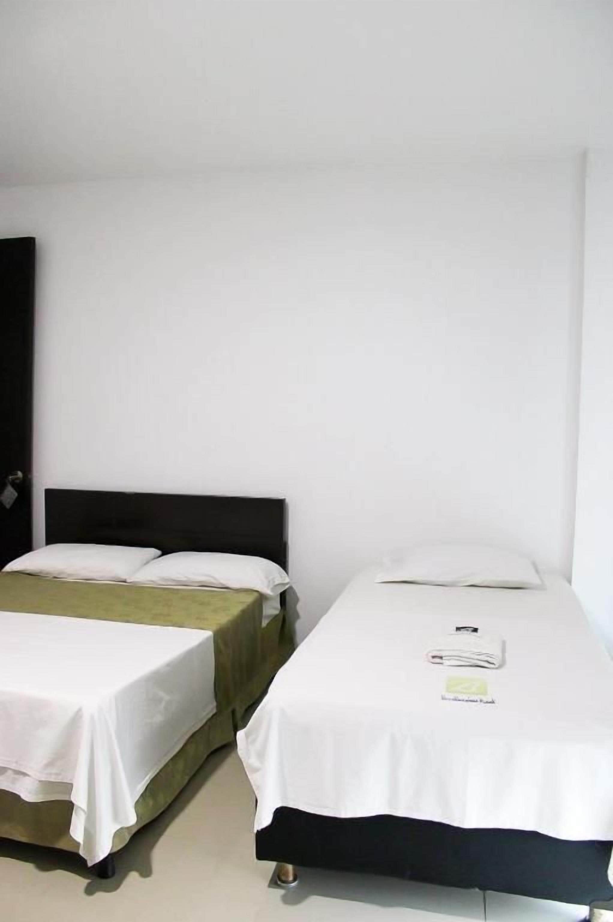 Zwei Einzelbetten mit weißer Bettwäsche, ein dunkles Kopfbrett und eine grüne Decke auf einem Bett.