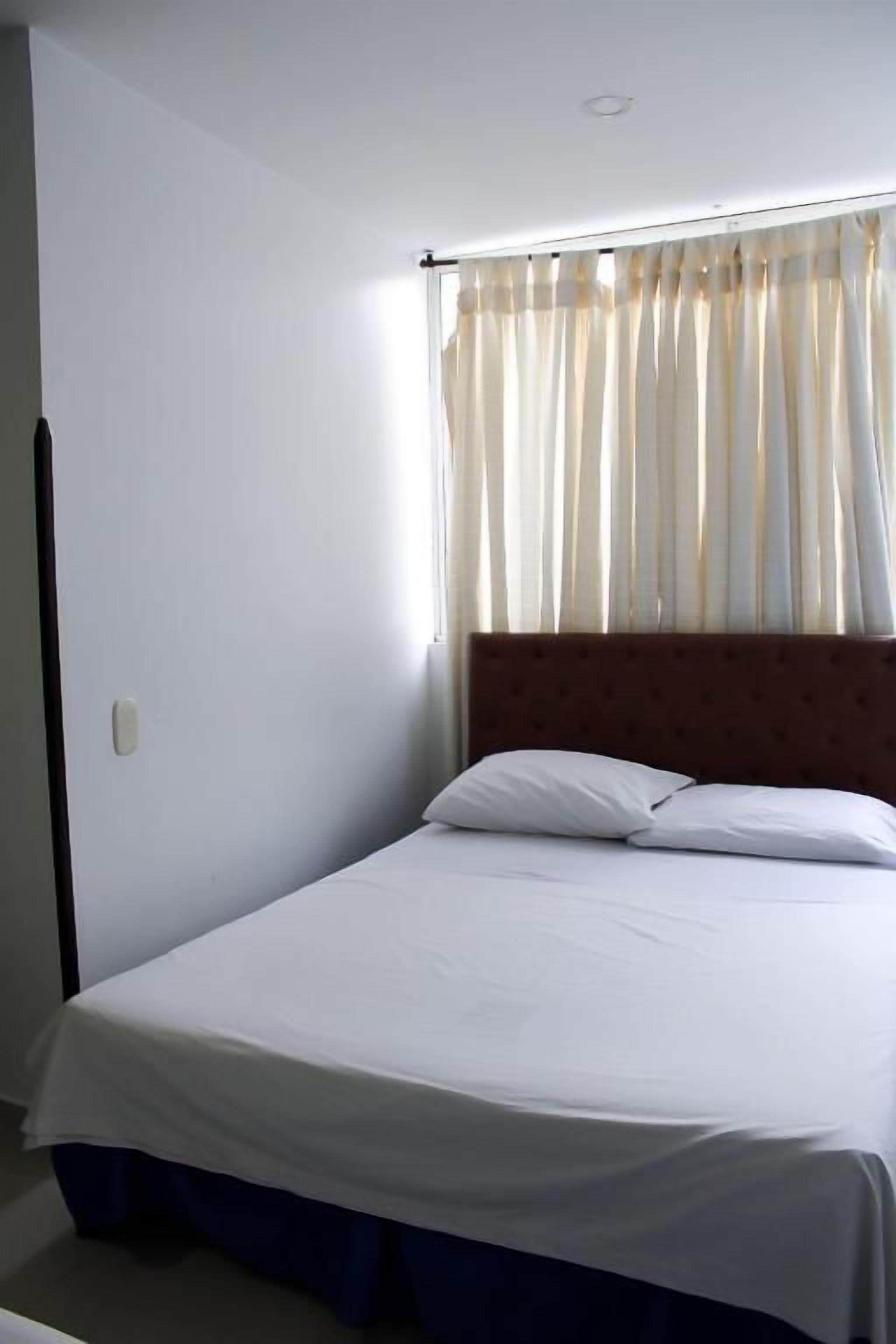 A single bed with a wooden headboard, white bedding, and a window with sheer curtains.