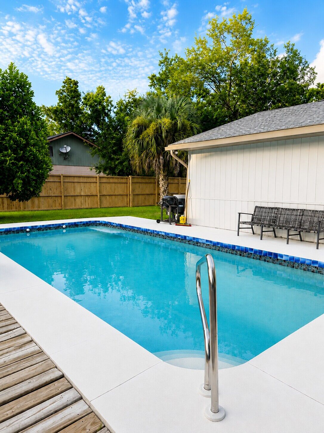 A swimming pool with a wooden deck, a covered patio area, and a fenced backyard.