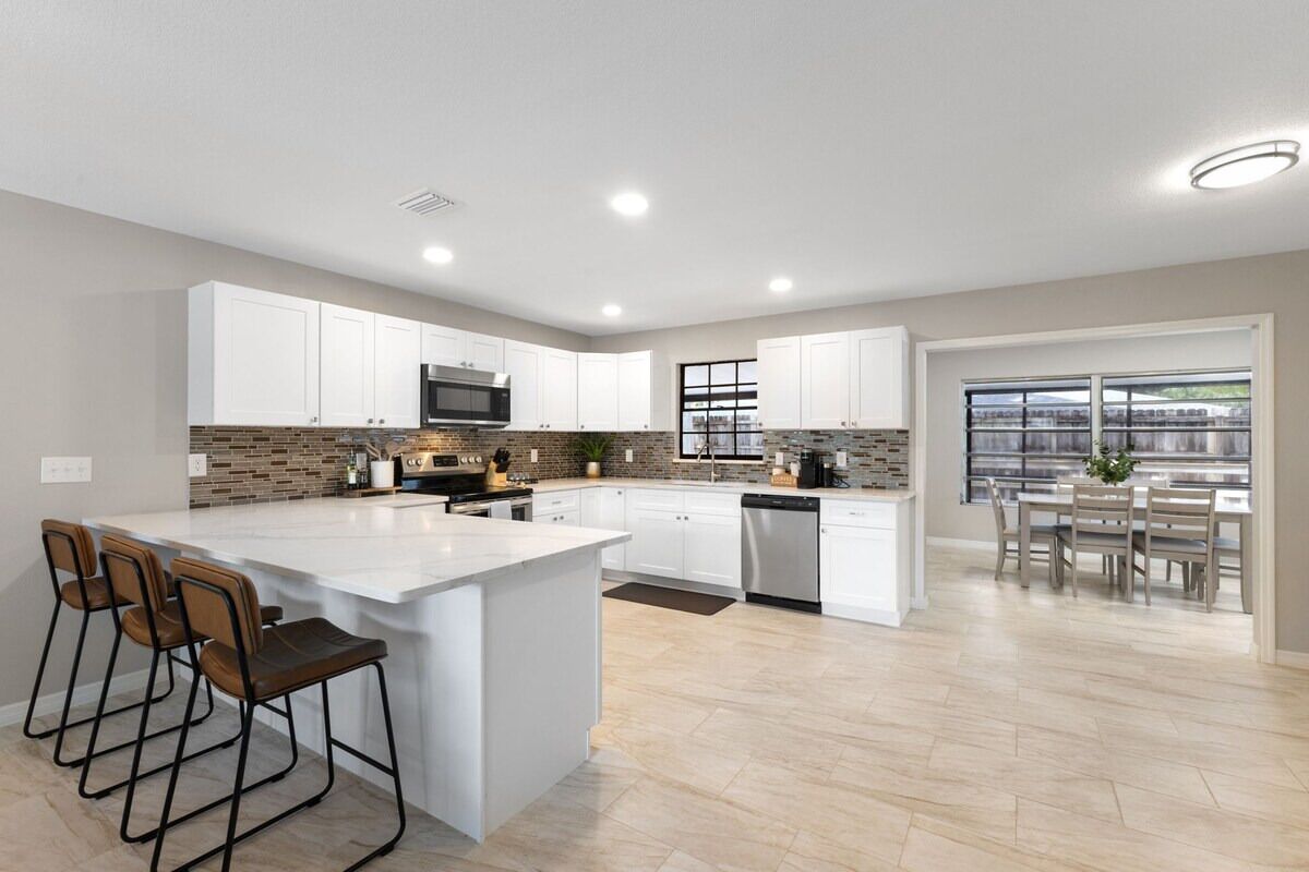 A modern kitchen with white cabinets, a central island, and a dining area with a view.
