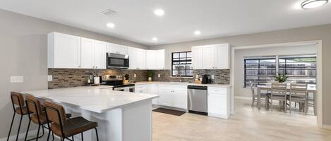 A modern kitchen with white cabinets, a central island, and a dining area with a view.