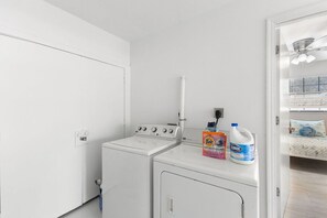 Ein Waschbereich mit Waschmaschine und Trockner, einem Deckenventilator und einem Bett mit Fenster.