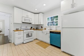 A modern kitchen with white cabinets, a stove, a dishwasher, and a window with a view. - 3BR Home Near BeltLine (Atlanta)