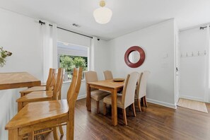 A dining area with a wooden table and chairs, a round mirror on the wall, and a view through a window. - 3BR Home Near BeltLine (Atlanta)