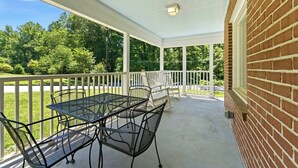 En overdækket terrasse med bord og stole, en murstensvæg og udsigt over et grønt landskab.