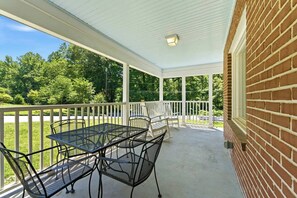 A covered patio with a table and chairs, a brick wall, and a view of a green landscape. - 3BR Home Near BeltLine (Atlanta)
