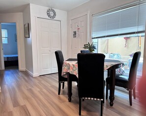 A dining area with a table set for four, flanked by two chairs, a clock on the wall, and a window with blinds. - Professional Rental Suite (Penticton)