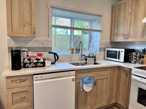 A kitchen with wooden cabinets, a coffee station, a microwave, and a dishwasher. - Professional Rental Suite (Penticton)