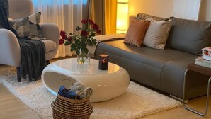 A living room with a sofa, a coffee table, and a lamp. - Stylish flat close to Basel with a stunning view (Weil am Rhein)
