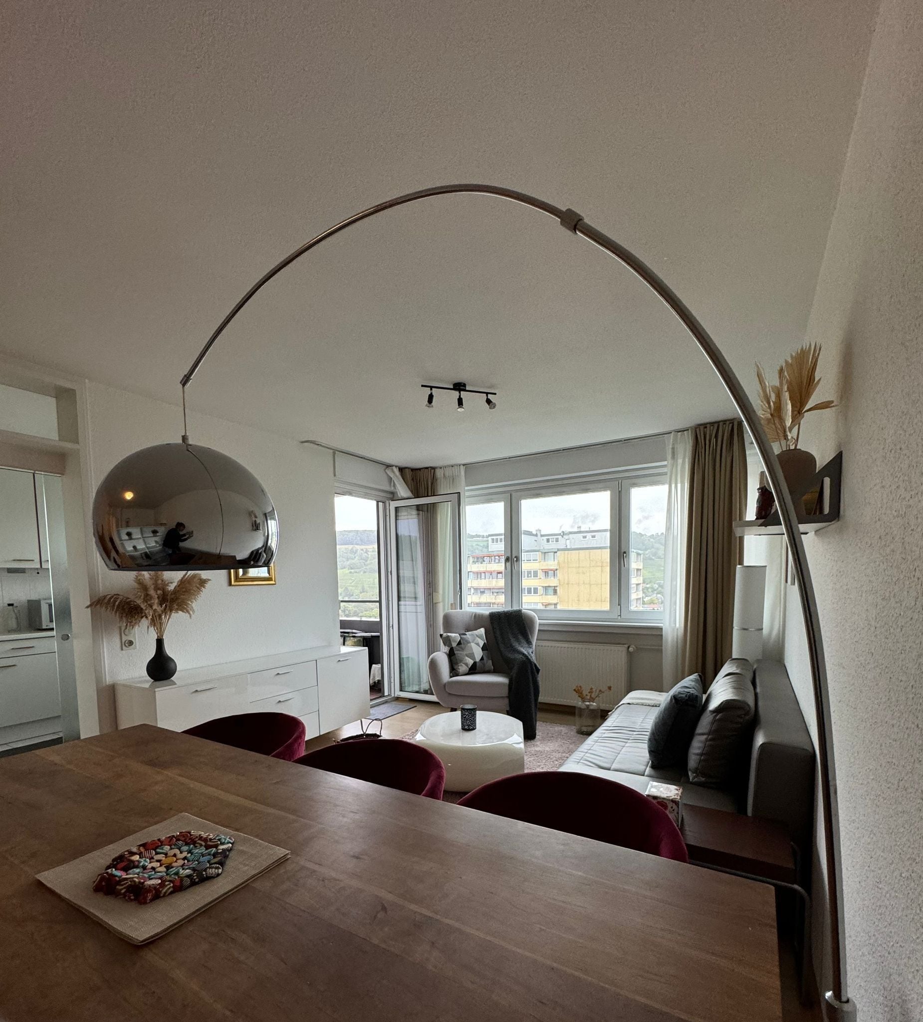 A modern living room with a dining area, a large window, and a ceiling light fixture.