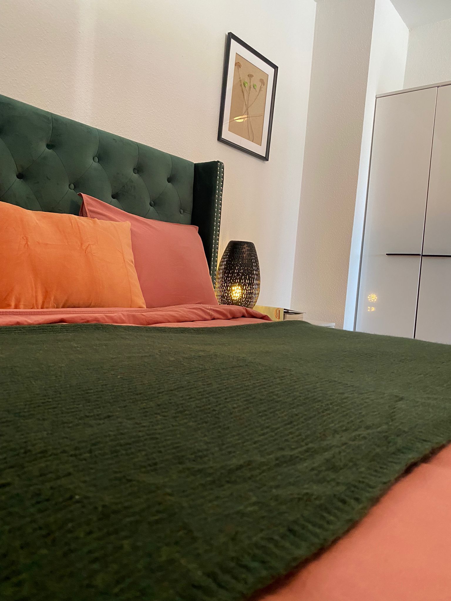 A bed with a green headboard, orange and pink pillows, and a textured green bedspread.