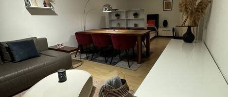 Una sala de estar moderna con un sofá, una mesa de centro, un área de comedor con una mesa y sillas, y una cocina con armarios y un lavamanos.