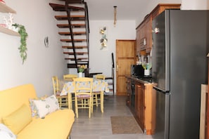 Un espacio habitable compacto con sofá, mesa de comedor, sillas, una zona de cocina con refrigerador y una escalera.
