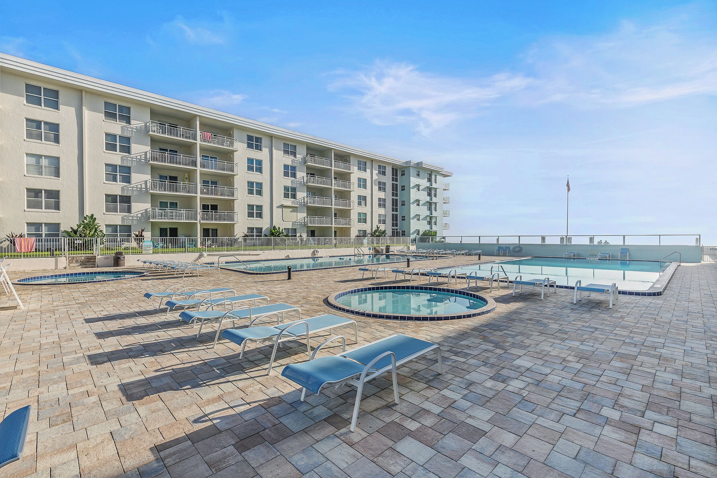 A hotel with multiple balconies, a swimming pool, and lounge chairs.