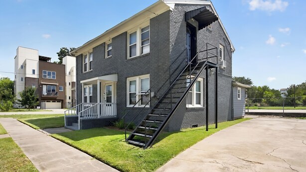 A two-story residential building with a front porch, a staircase, and a small front yard. - Blue Luxe Getaway Stylish 2BR Near Downtown (Houston)