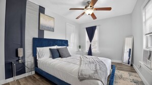 A bedroom with a bed, a ceiling fan, a window with curtains, a mirror, and a bedside table. - Blue Luxe Getaway Stylish 2BR Near Downtown (Houston)