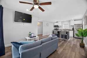 A modern living room with a grey sofa, a flat-screen TV, and a ceiling fan. - Blue Luxe Getaway Stylish 2BR Near Downtown (Houston)