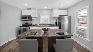 A modern kitchen with white cabinets, stainless steel appliances, a granite countertop, and a window with blinds. - Blue Luxe Getaway Stylish 2BR Near Downtown (Houston)