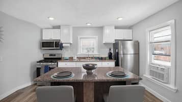 Una cocina moderna con armarios blancos, electrodomésticos de acero inoxidable, encimera de granito y una ventana con persianas.
