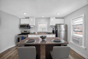 A modern kitchen with white cabinets, stainless steel appliances, a granite countertop, and a window with blinds. - Blue Luxe Getaway Stylish 2BR Near Downtown (Houston)