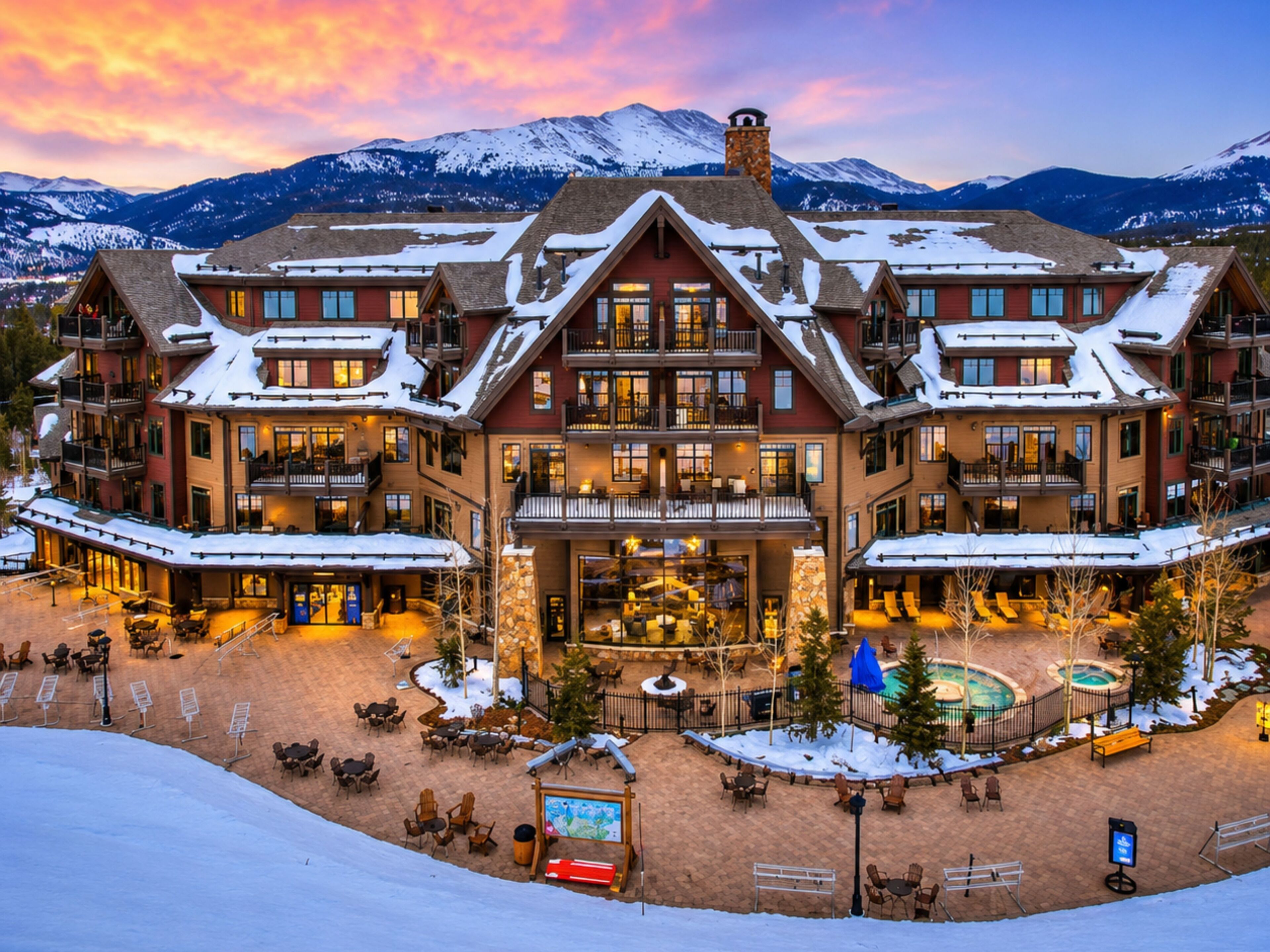 Ein mehrstöckiges Chalet mit Skipiste im Vordergrund, einem Poolbereich und einer Bergkulisse.