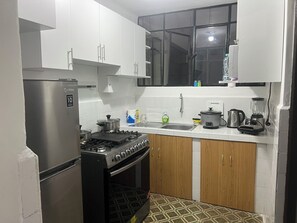 Eine kompakte Küche mit weißen Schränken, einem Edelstahlkühlschrank, einer Gasherdplatte und einem Einbauofen.