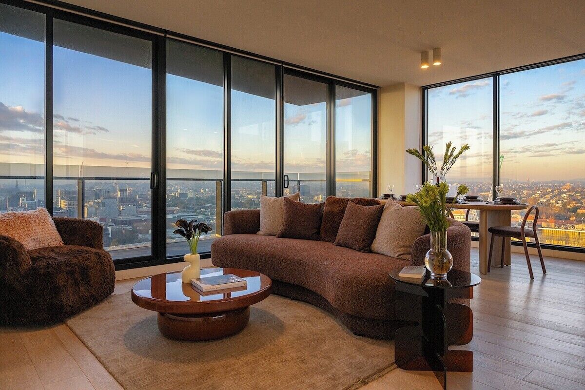 A modern living room with a large window, a brown sofa, a coffee table, and a small side table with a vase.