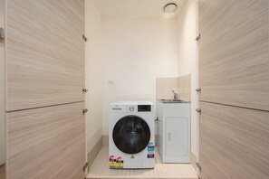 Une petite buanderie équipée d’un lave-linge à chargement frontal et d’un meuble de rangement.