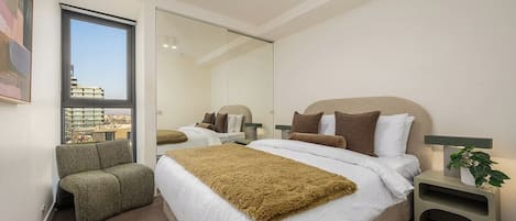 A modern hotel room with a large bed, a seating area, and a view through a glass door.