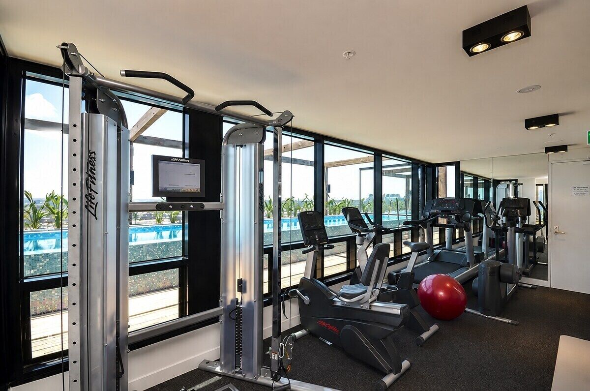 A gym with cardio machines, weightlifting equipment, and a large window offering a view of a pool.