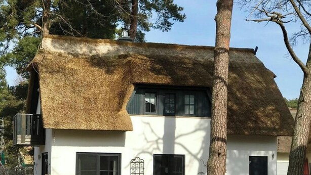 Uma casa com telhado de palha, janelas amplas e porta de garagem aparente.