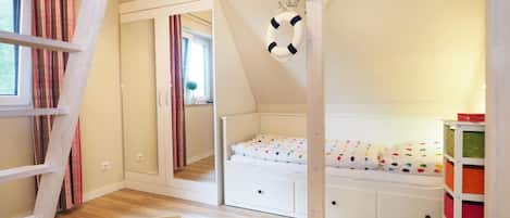 A child's bedroom with a loft bed, wooden flooring, a bookshelf, and a small window.