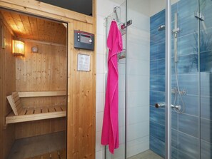 Eine Sauna mit Holzwänden und Bedienfeld, eine Duschkabine mit blauen Kacheln und ein rosa Handtuch auf einem Wäscheständer.