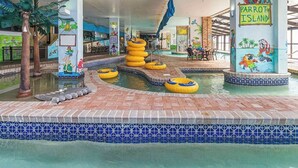 An indoor pool area with multiple water slides and inflatable rings, surrounded by tiled walls and a mural of parrots. - Oceanfront Paradise Getaway (Myrtle Beach)